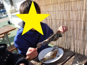 焼き魚が刺さった串をもつ児童
